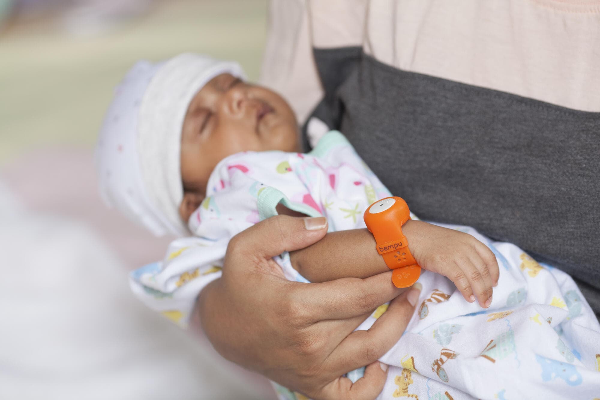 A mother holding her sleeping newborn wearing a BEMPU TempWatch bracelet